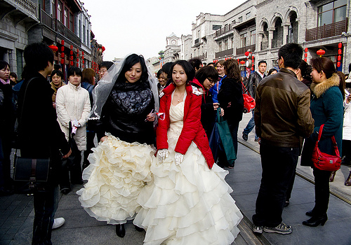 两位女同性恋者穿着婚纱走在前门大街，引来路人关注目光。